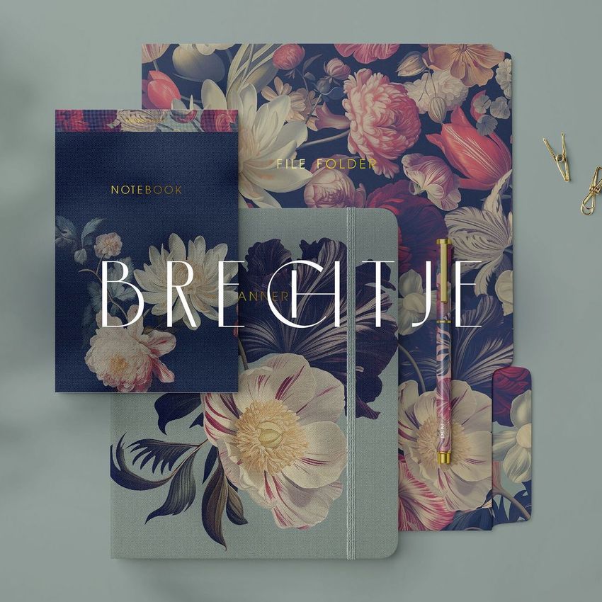 Stationery set mockup featuring a notebook, file folder, and planner with floral patterns arranged on a gray surface.