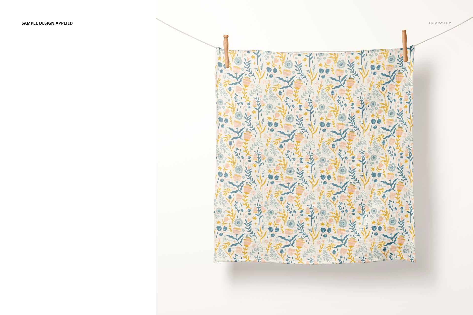 Front view of a crinkle muslin swaddle blanket mockup featuring a soft botanical print, clipped to a line.