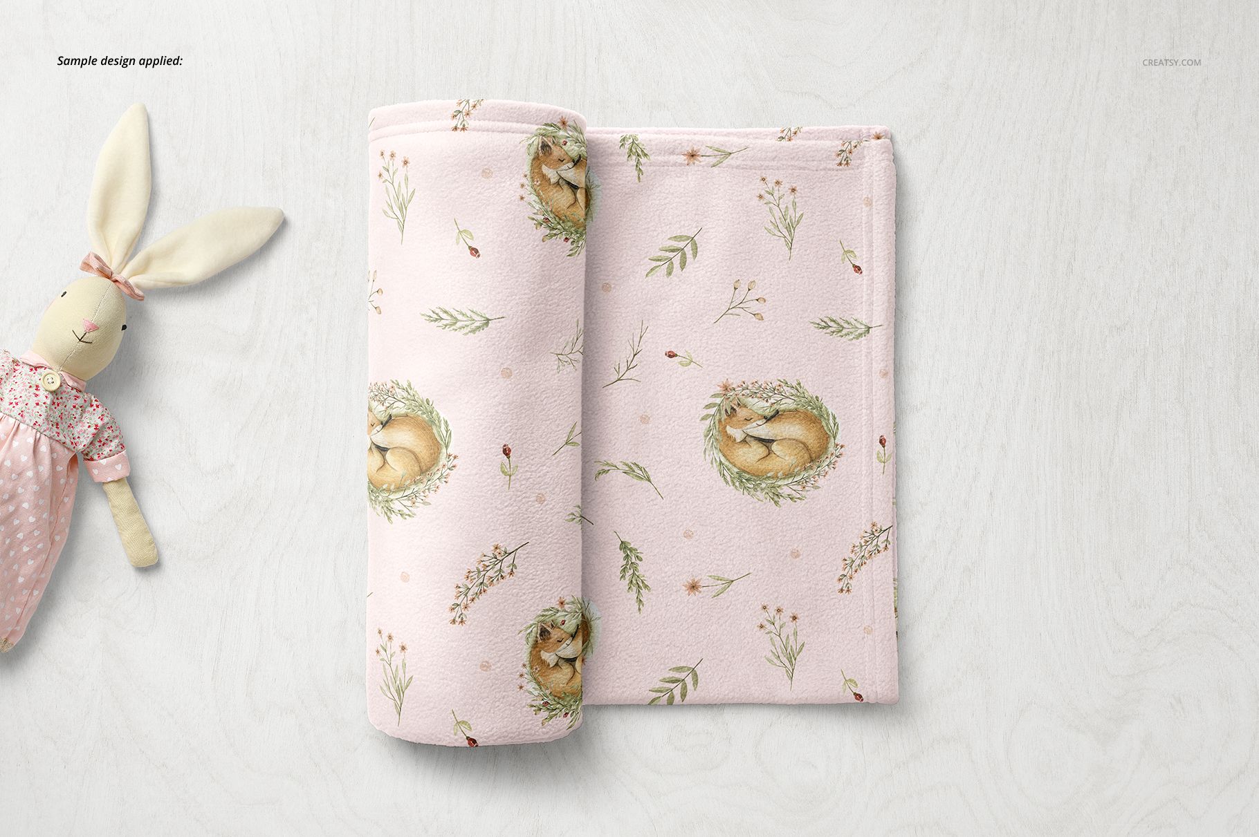 PSD mockup of a soft fleece baby blanket with gentle floral and animal motifs, presented on a light wood background.