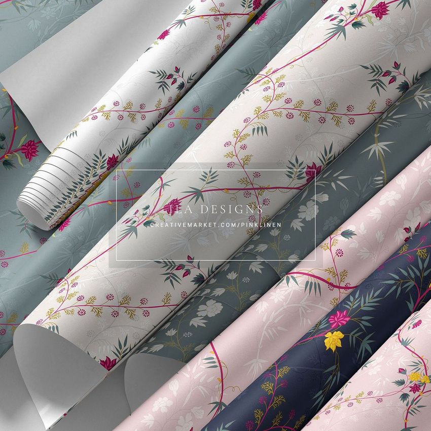 Paper wallpaper mockup showing several rolled sheets with floral patterns in shades of white, blue, pink, and navy on a flat surface.