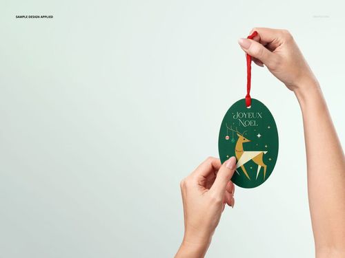 Christmas oval ornament mockup featuring a green surface with gold reindeer and stars, held by a red ribbon.