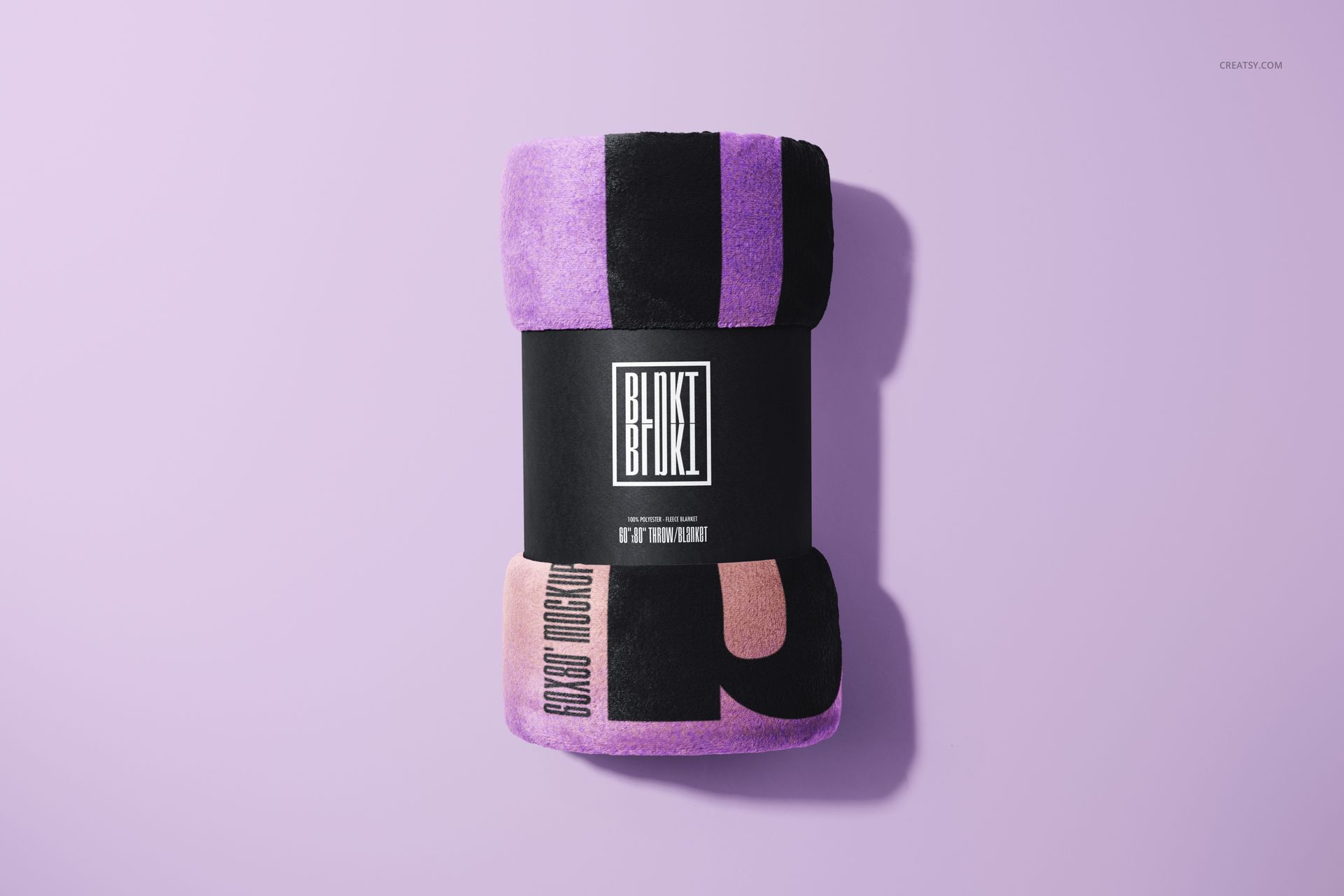 Fleece blanket mockup rolled and wrapped in a black label, featuring purple and pink blocks on a light purple surface.