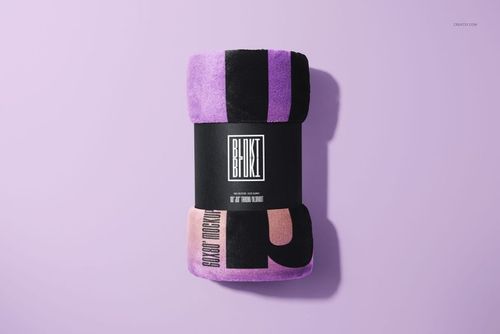 Fleece blanket mockup rolled and wrapped in a black label, featuring purple and pink blocks on a light purple surface.