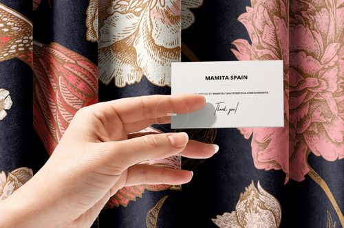 PSD mockup showing a hand holding a business card near richly patterned dark fabric with oversized flowers and gold accents.