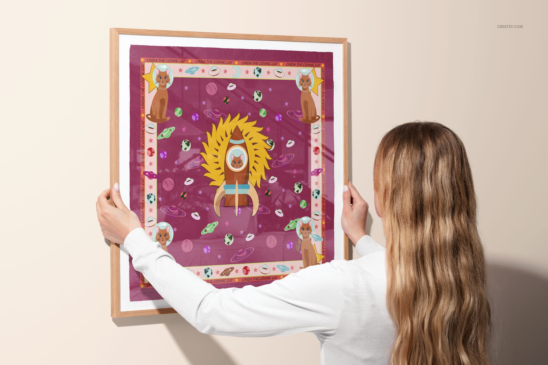 Framed silk scarf mockup showing a colorful design with central yellow motif and decorative border, held against a wall.
