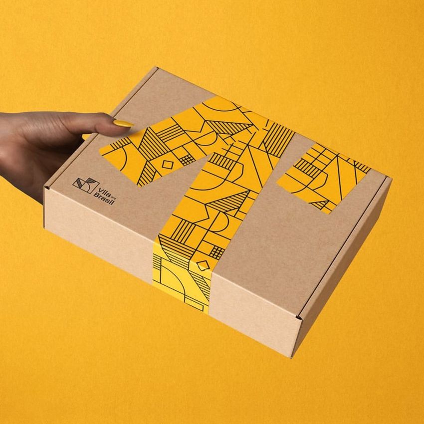 Hand holding a mailing box mockup with a geometric yellow and black pattern on the lid, set against a solid yellow background.