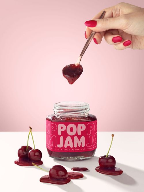 Cherry jam jar mockup with bold pink packaging, open lid, dripping jam, and cherries on a white surface.