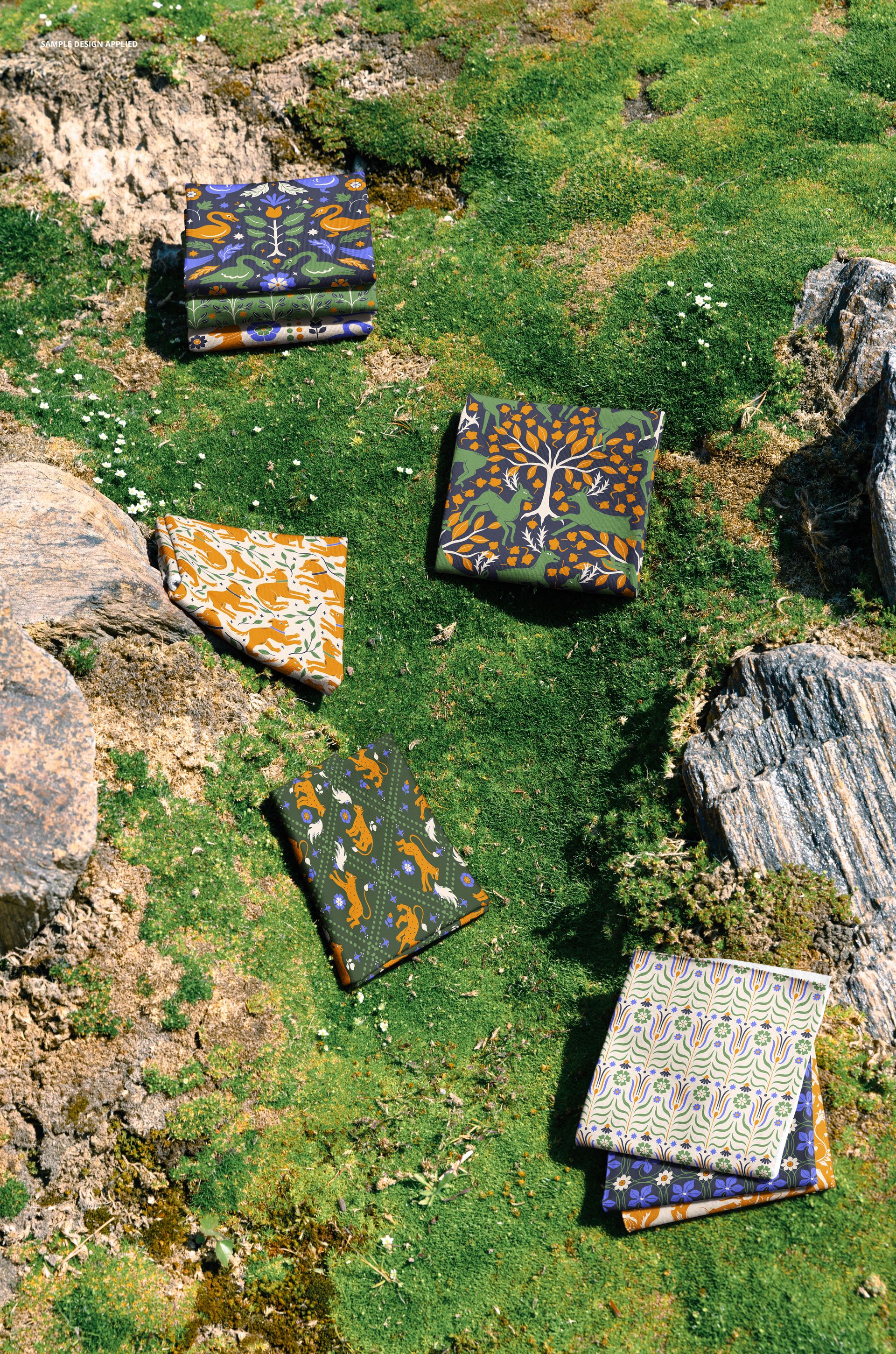 PSD mockup showing multiple folded fabrics in various designs placed on natural moss and stone surface.