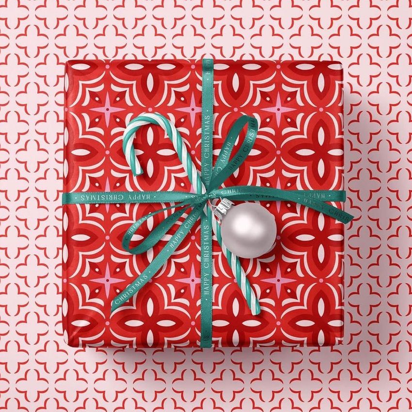 Christmas gift mockup featuring a red patterned box with green ribbon, candy cane, and silver ornament on a matching background.