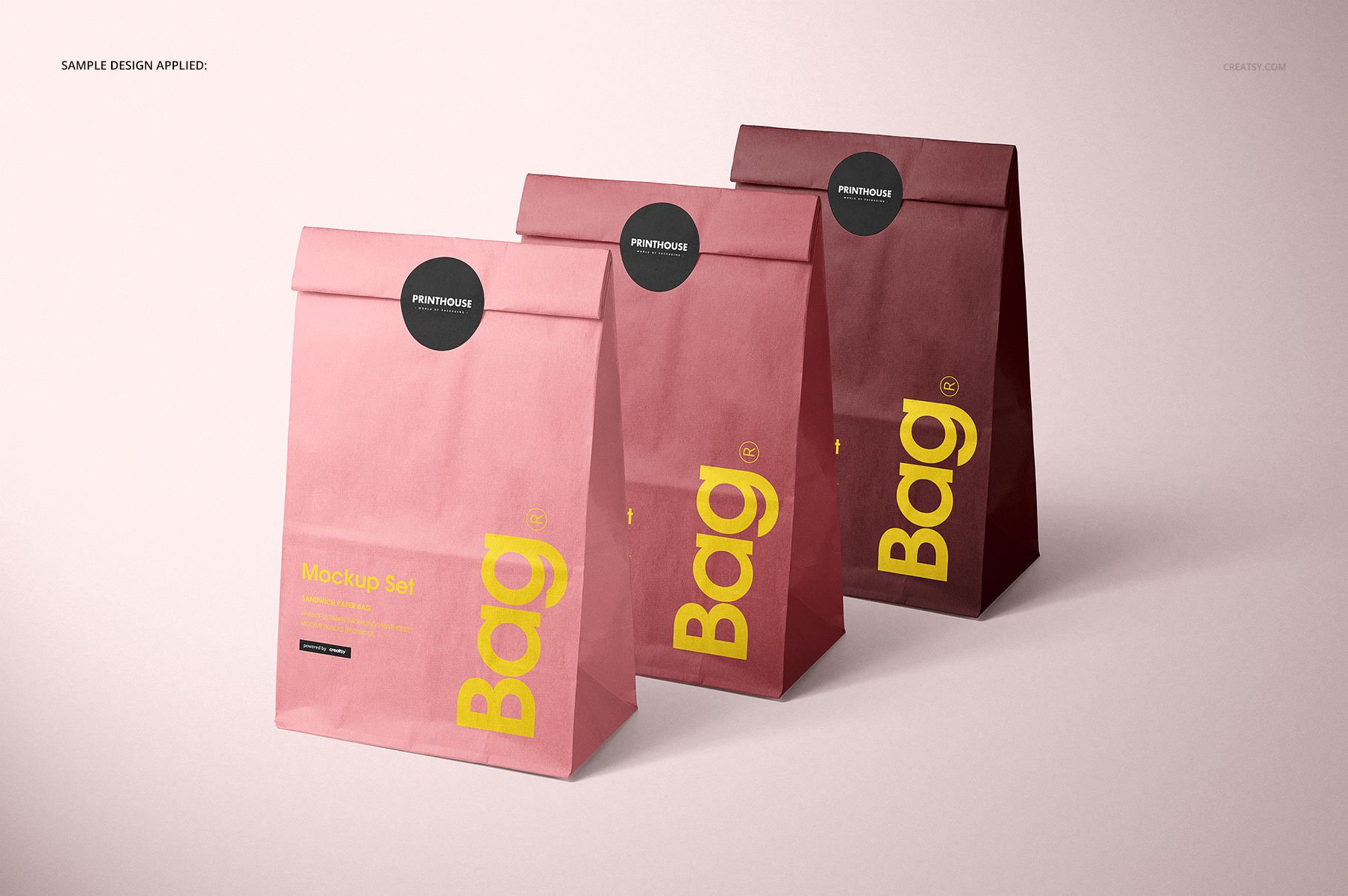 PSD mockup showing three upright lunch bags in different pink hues, featuring simple labels and a soft gradient backdrop.