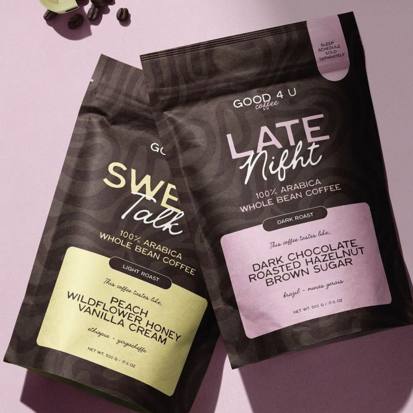 Coffee branding mockup featuring two upright coffee bags with text overlays, set on a pink surface with scattered coffee beans.