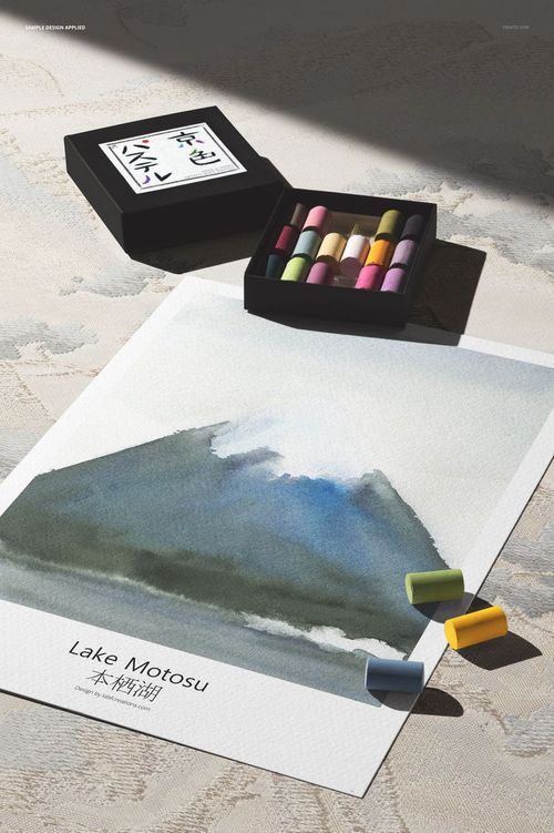 Vertical poster print mockup with a watercolor mountain scene, Japanese text, and pastel sticks in a black box nearby.