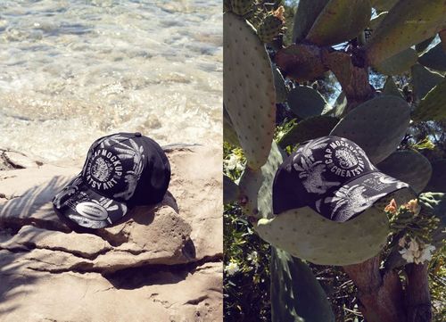 PSD mockup of a black snapback cap with white print, placed on natural surfaces including a rock and cactus outdoors.