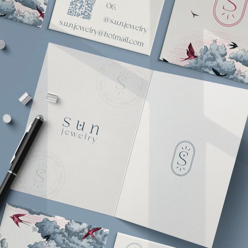 Folded card mockup on a blue surface, featuring minimal text, a pen, and cards with blue and pink cloud illustrations.