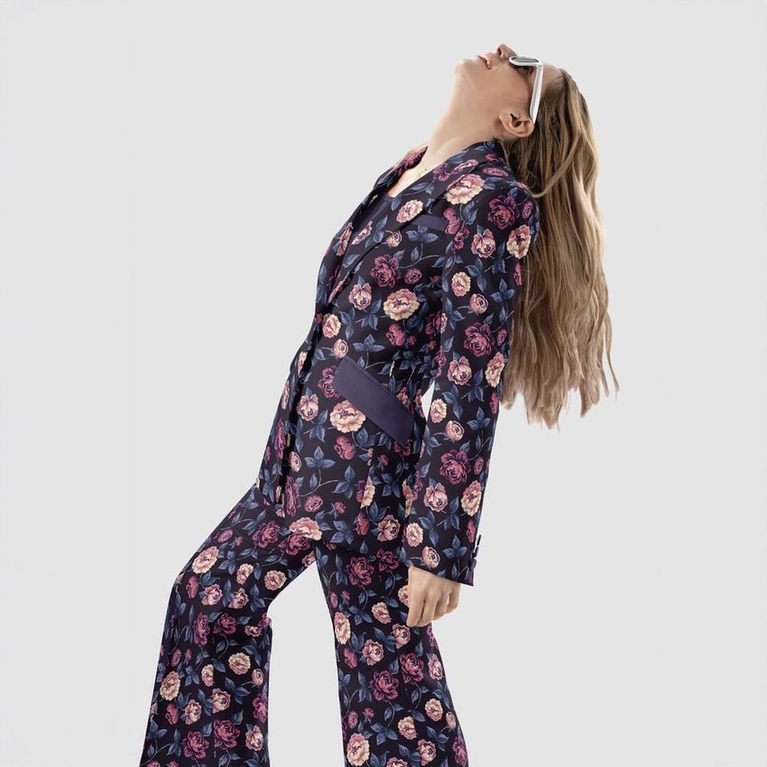 Woman wearing a two-piece blazer and trousers mockup set with a dark floral peony pattern, posing against a plain light background.
