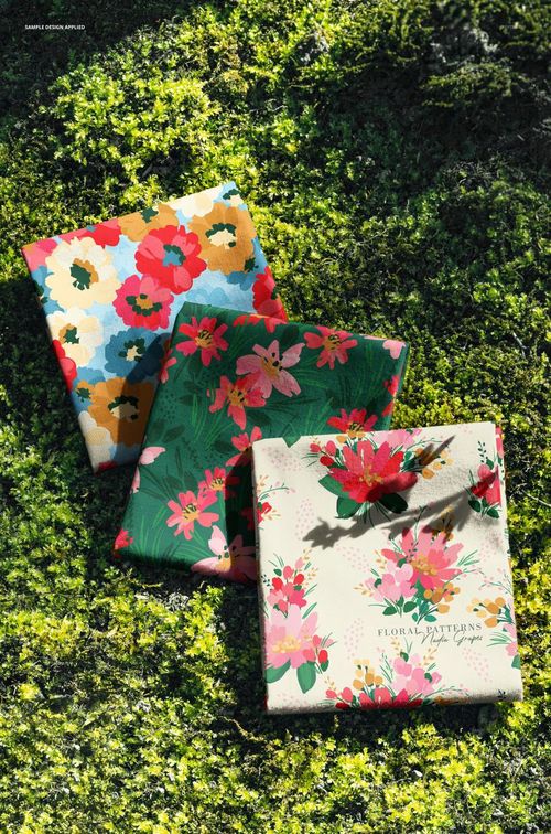 PSD mockup showing three fabric squares with bold flower prints placed on natural green moss in sunlight.