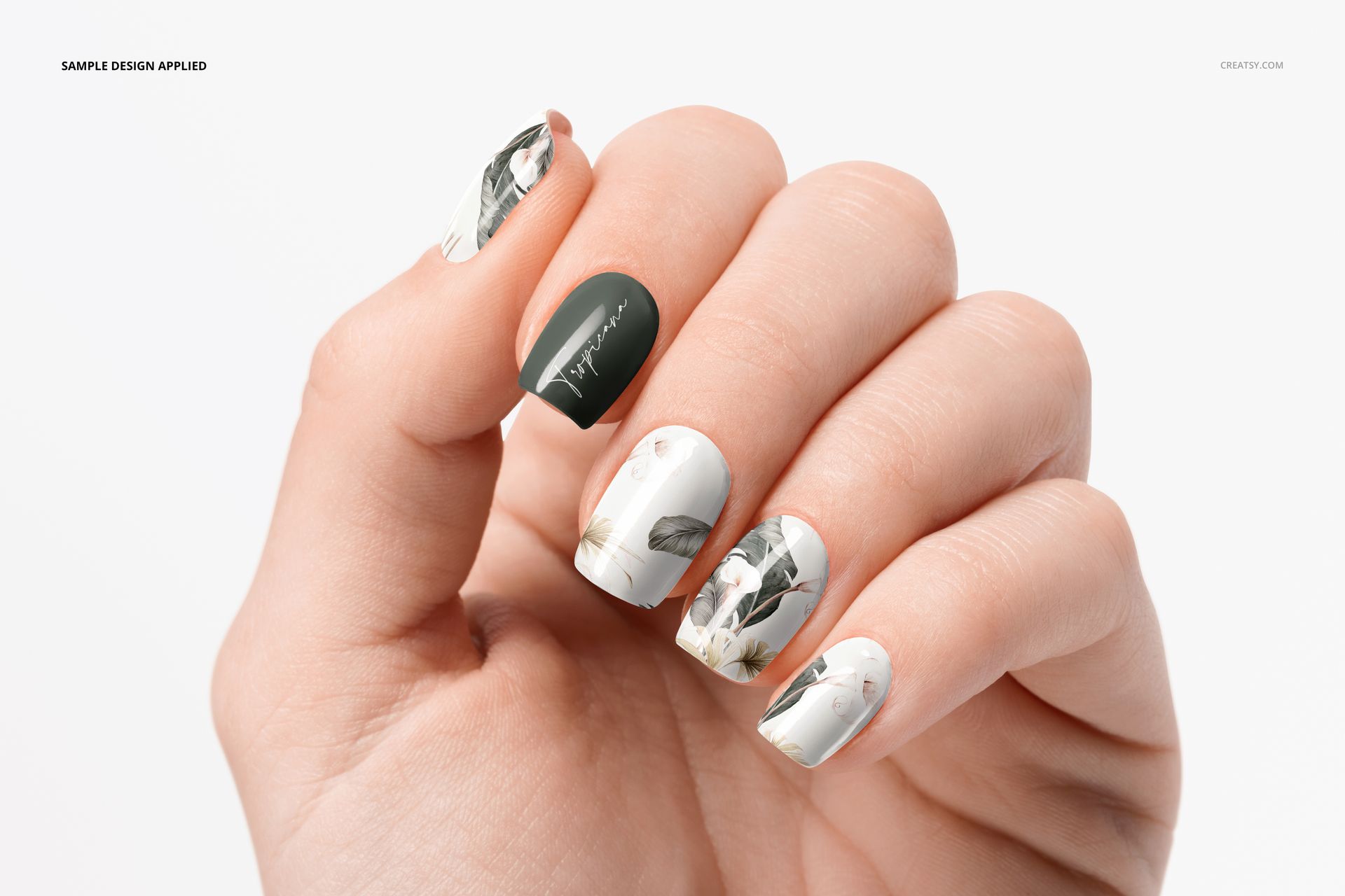Close-up of a hand showing squoval nails mockup with botanical designs and solid green accent nail on a white background.
