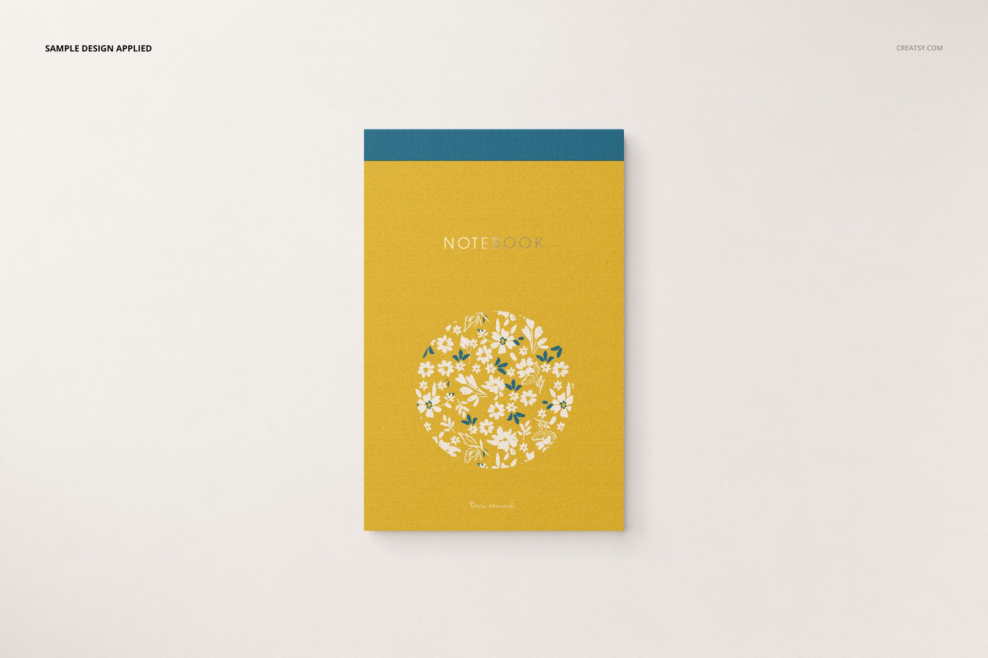 Stationery mockup showing a notebook with a yellow cover, blue top edge, and circular white flower design in the center.