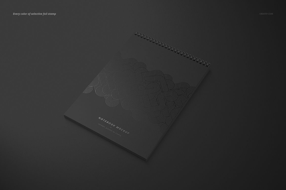 Angled view of a black A4 spiral notebook mockup with geometric embossed design, placed on a matte dark background.
