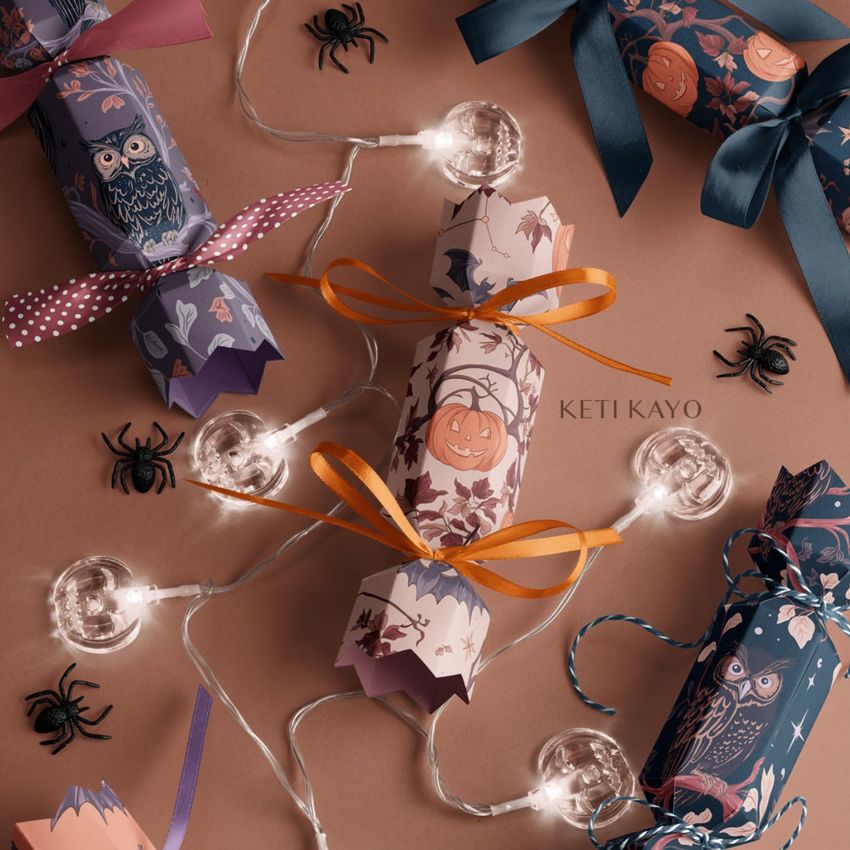 Halloween party cracker packaging mockup featuring illustrated crackers with pumpkins, owls, and autumn patterns on a brown surface.