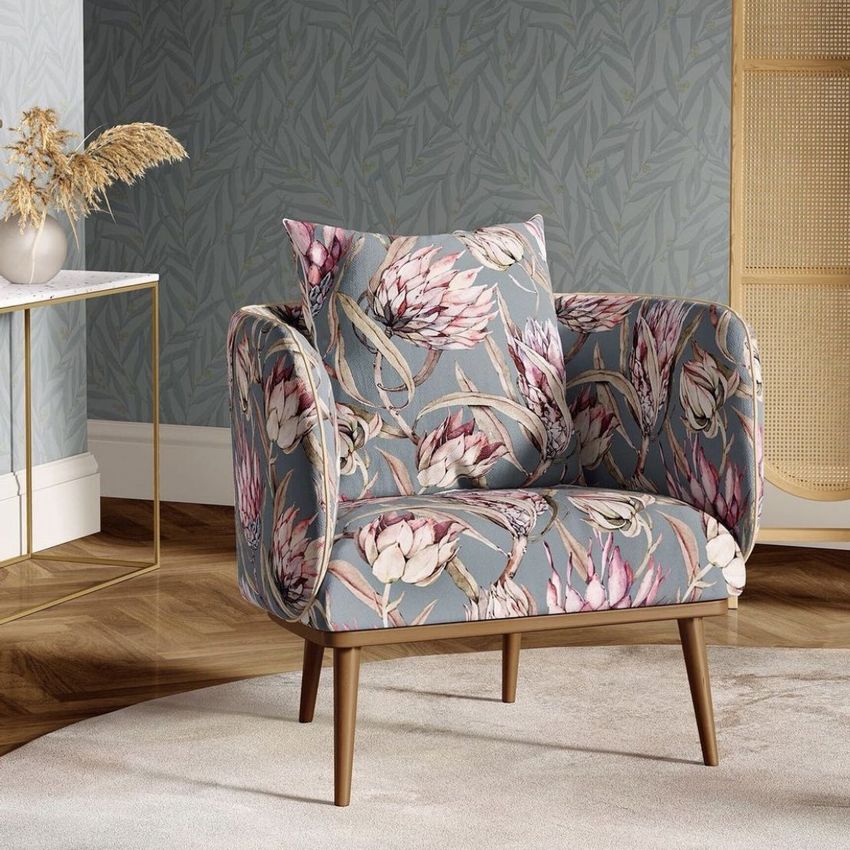 Armchair mockup in a sitting corner, upholstered with a protea floral pattern, set on a round rug with a leafy wallpaper background.