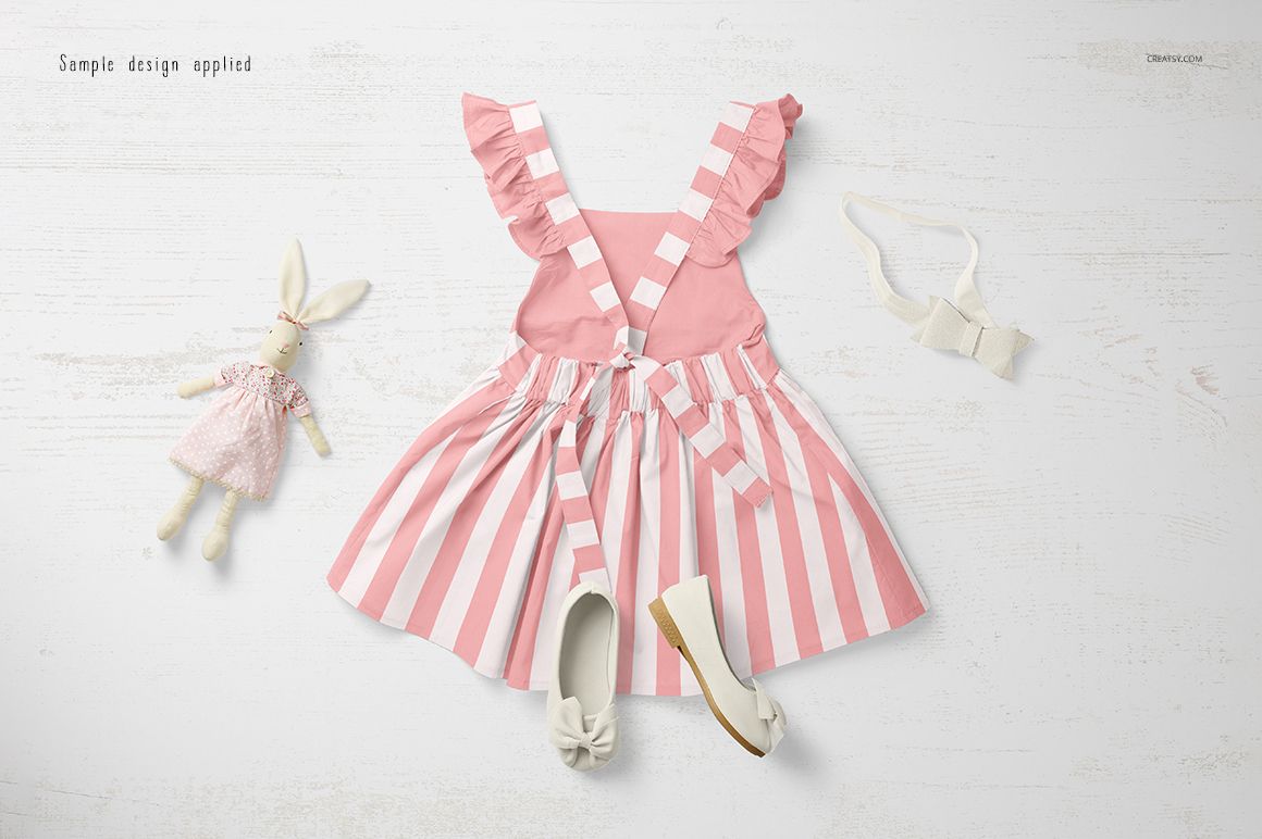 Front view of a pink and white striped baby dress mockup with ruffled straps, displayed on a light wooden surface.