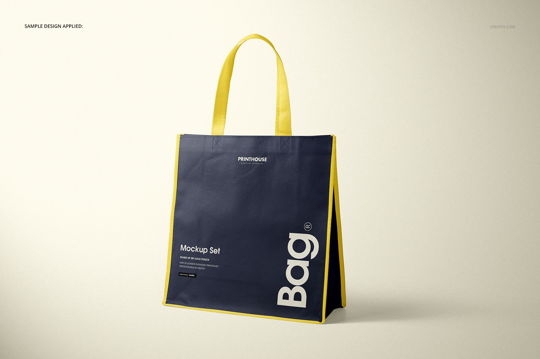 Front view of a non-woven tote bag mockup with navy blue panels, yellow handles and edges, standing on a light surface.
