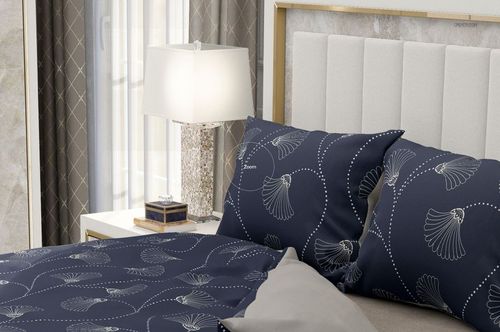 Mockup of a bedroom scene displaying navy blue patterned bedding and pillows beside a white lamp and nightstand.
