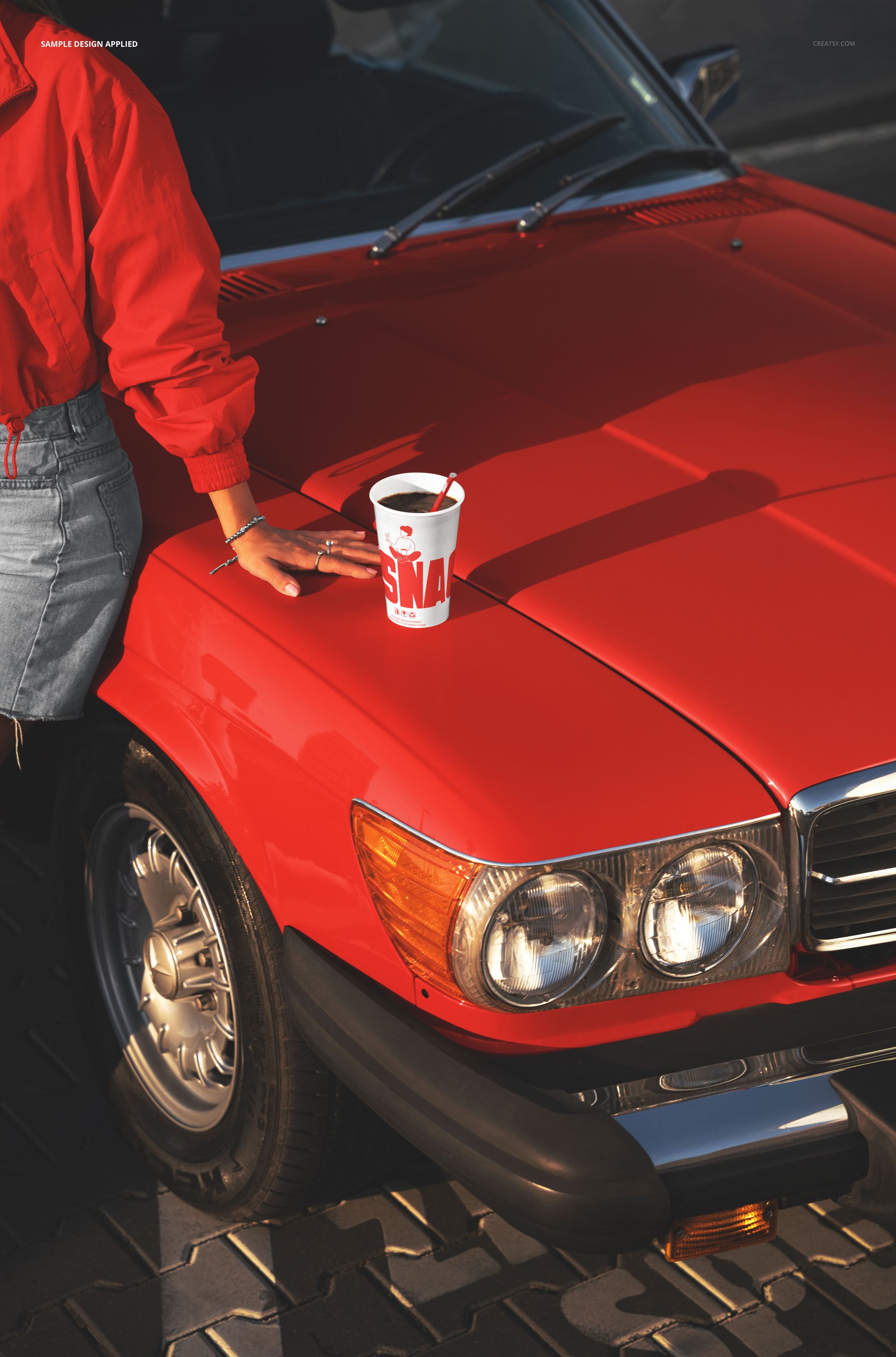 PSD mockup featuring a takeaway beverage cup on the shiny red hood of a vintage car, with a person standing nearby.