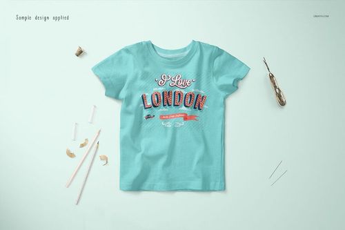 Baby t-shirt mockup in light blue, shown from above with decorative text and surrounded by crafting supplies.