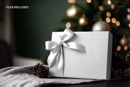 White gift box mockup with a shiny satin ribbon, set on a soft fabric with pine cones and blurred ornaments.