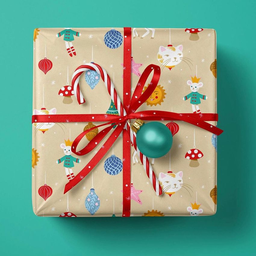 Christmas gift mockup featuring a square box wrapped in festive patterned paper with red ribbon, candy canes, and a teal ornament.