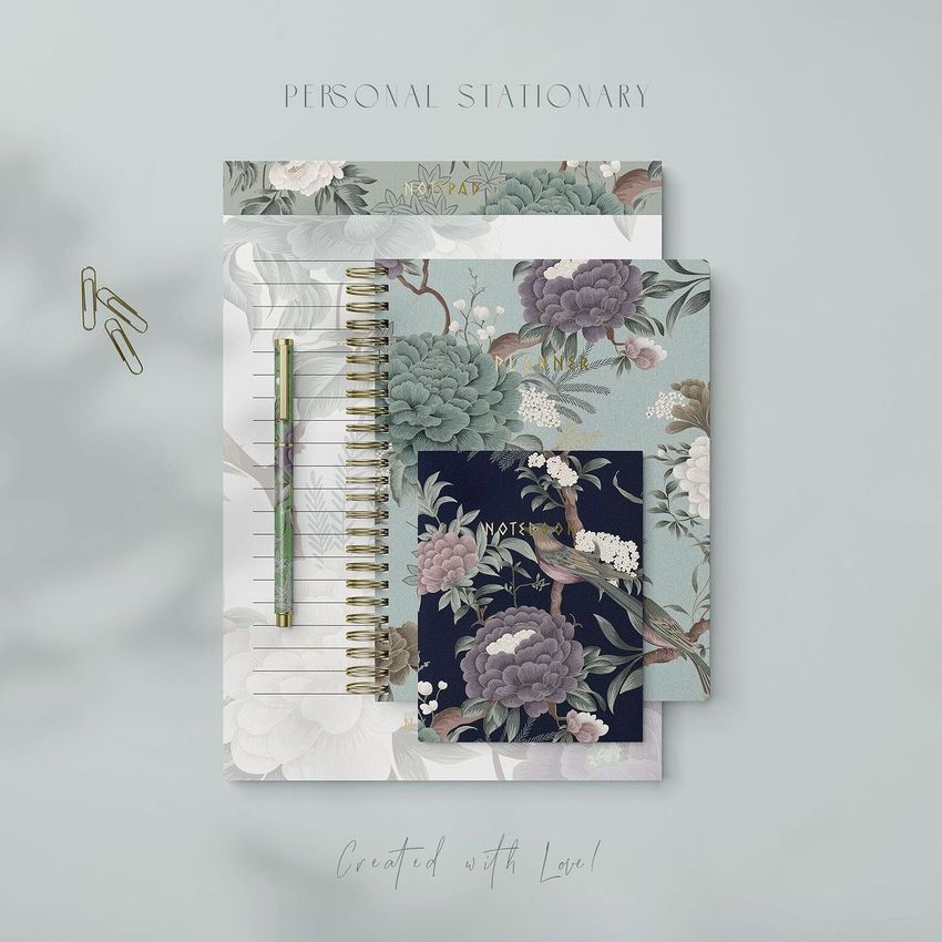 Stationery mockup featuring a spiral notebook, two cards, and a pen arranged on a light gray surface with floral designs.