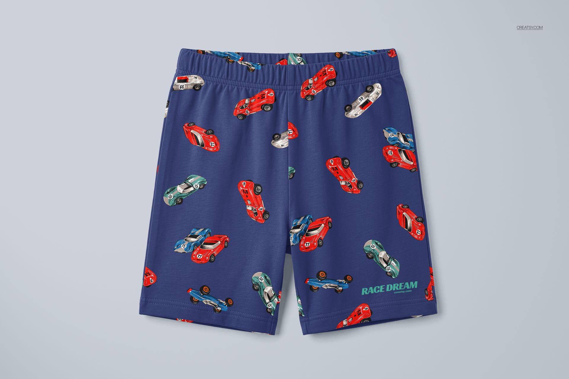 Kids short pyjamas mockup featuring a blue fabric with red, green, and blue cars in a repeating pattern, shown flat.