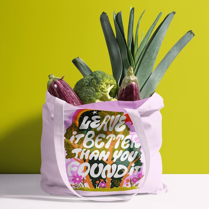 Tote bag mockup featuring a white bag with a colorful text overlay, filled with fresh vegetables against a yellow background.