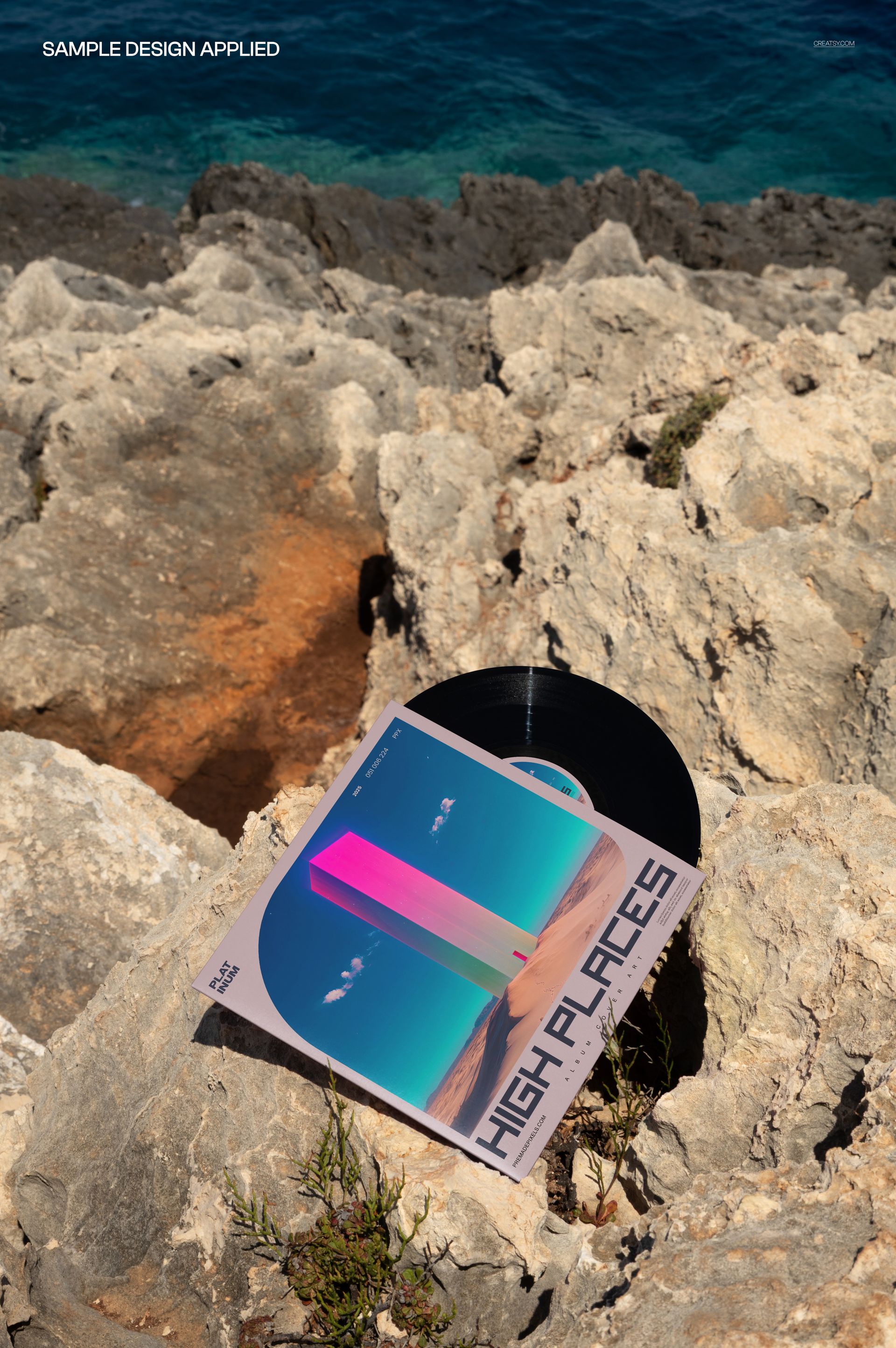 PSD mockup showing a vinyl record and modern album sleeve placed on natural stone with a scenic sea view behind.