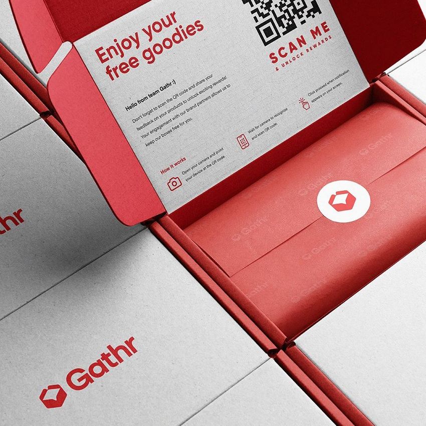 Mailing box mockup with a red interior, open to show printed instructions, QR code, and branded packaging on a stack of closed boxes.