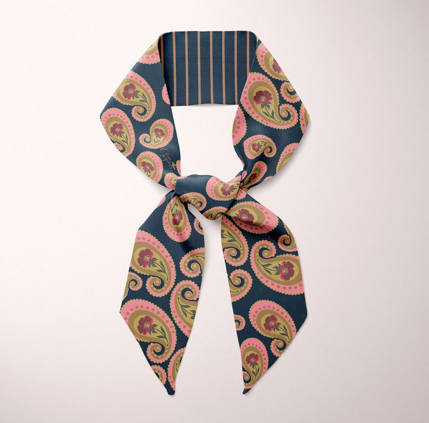 Top view of a tied twilly scarf mockup featuring a paisley pattern in green, pink, and beige on a dark background.