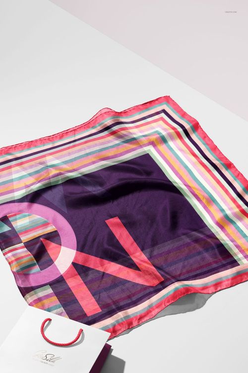 Mockup of a habotai silk scarf with multicolored stripes and large letters, laid out next to a paper bag.