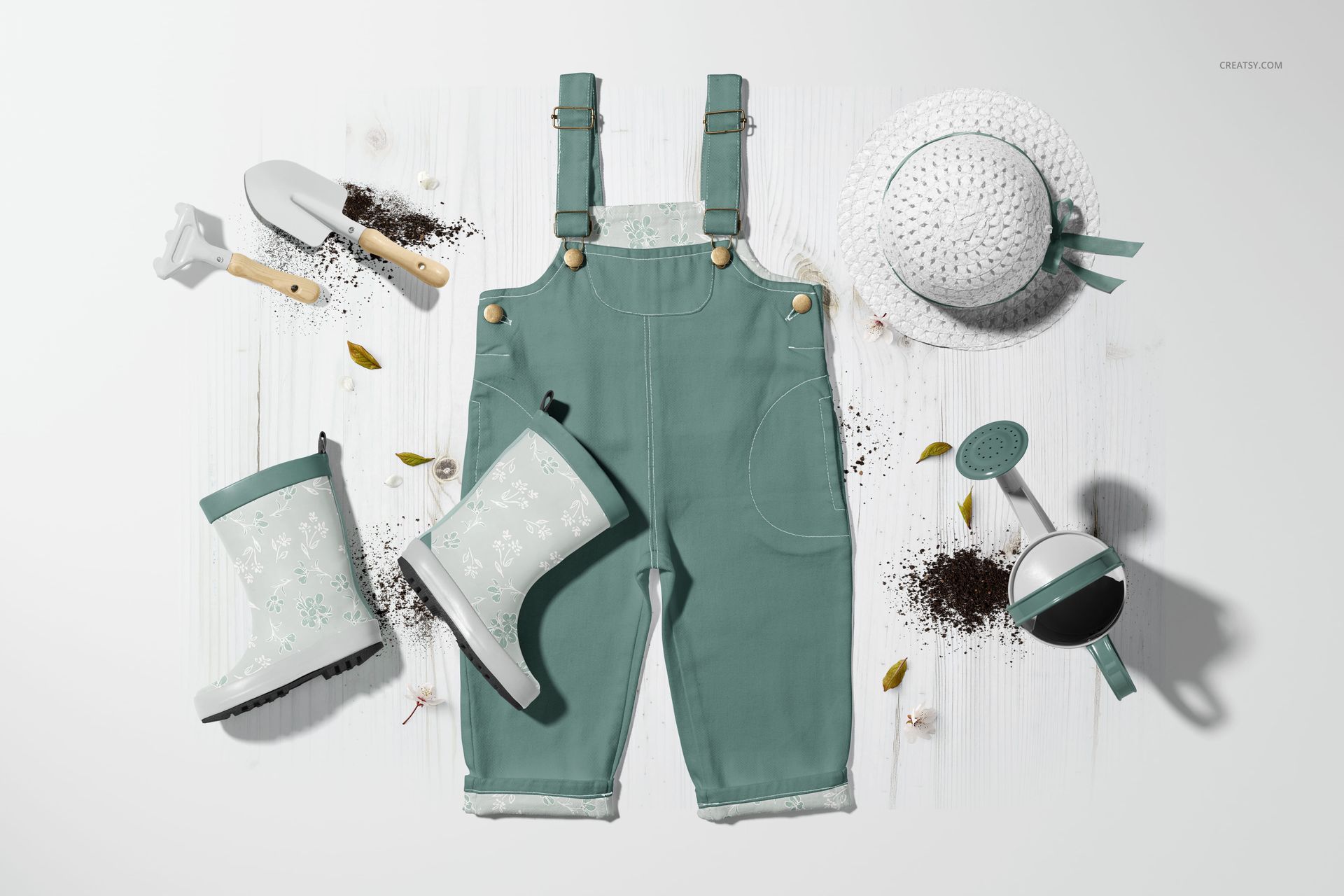 Front view of kids’ green dungarees mockup set, surrounded by gardening tools, boots, and a hat with ribbon detail.