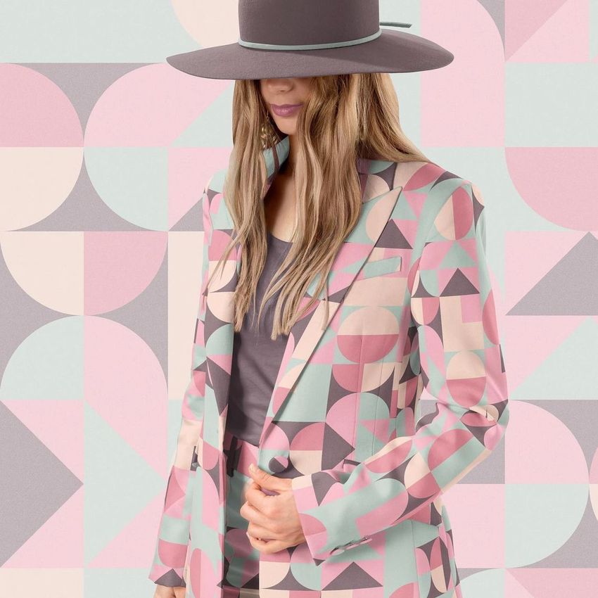 Adult apparel mockup showing a two-piece suit with pink, mauve, and mint geometric shapes, styled with a wide-brim hat.