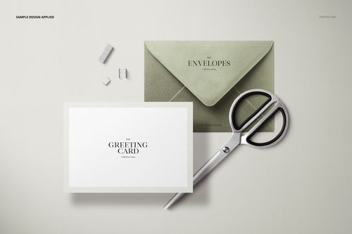 PSD mockup of a C6 envelope and greeting card in metallic green, arranged flat with scissors and paper clips nearby.