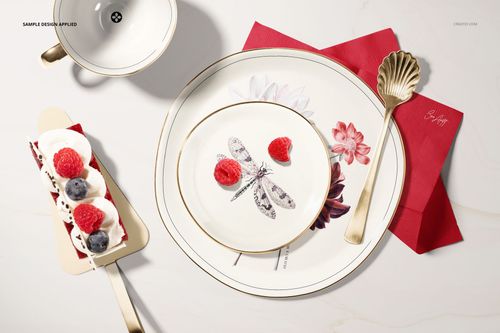 Top view of a plate mockup set with floral and dragonfly designs, gold utensils, and a dessert slice on a white background.