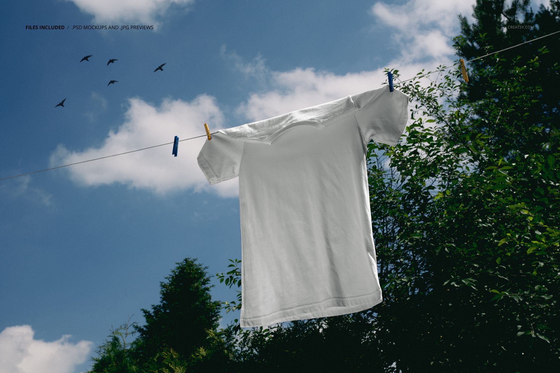 PSD mockup of a blank white T-shirt suspended on a rope, featuring a sky with clouds and trees in the scene.