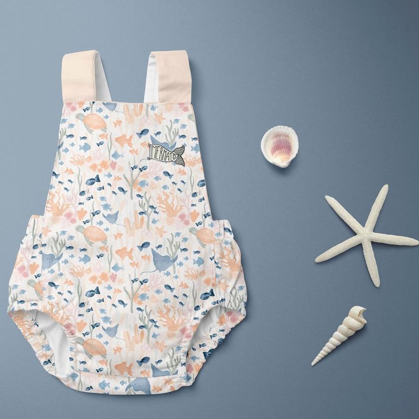 Baby romper mockup featuring a sea-themed pastel pattern, displayed flat on a blue background with seashell props.