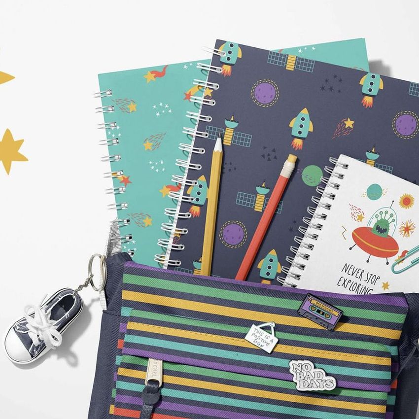 School backpack mockup with spiral notebooks featuring colorful space-themed designs, pencils, and a sneaker keychain on a white background.