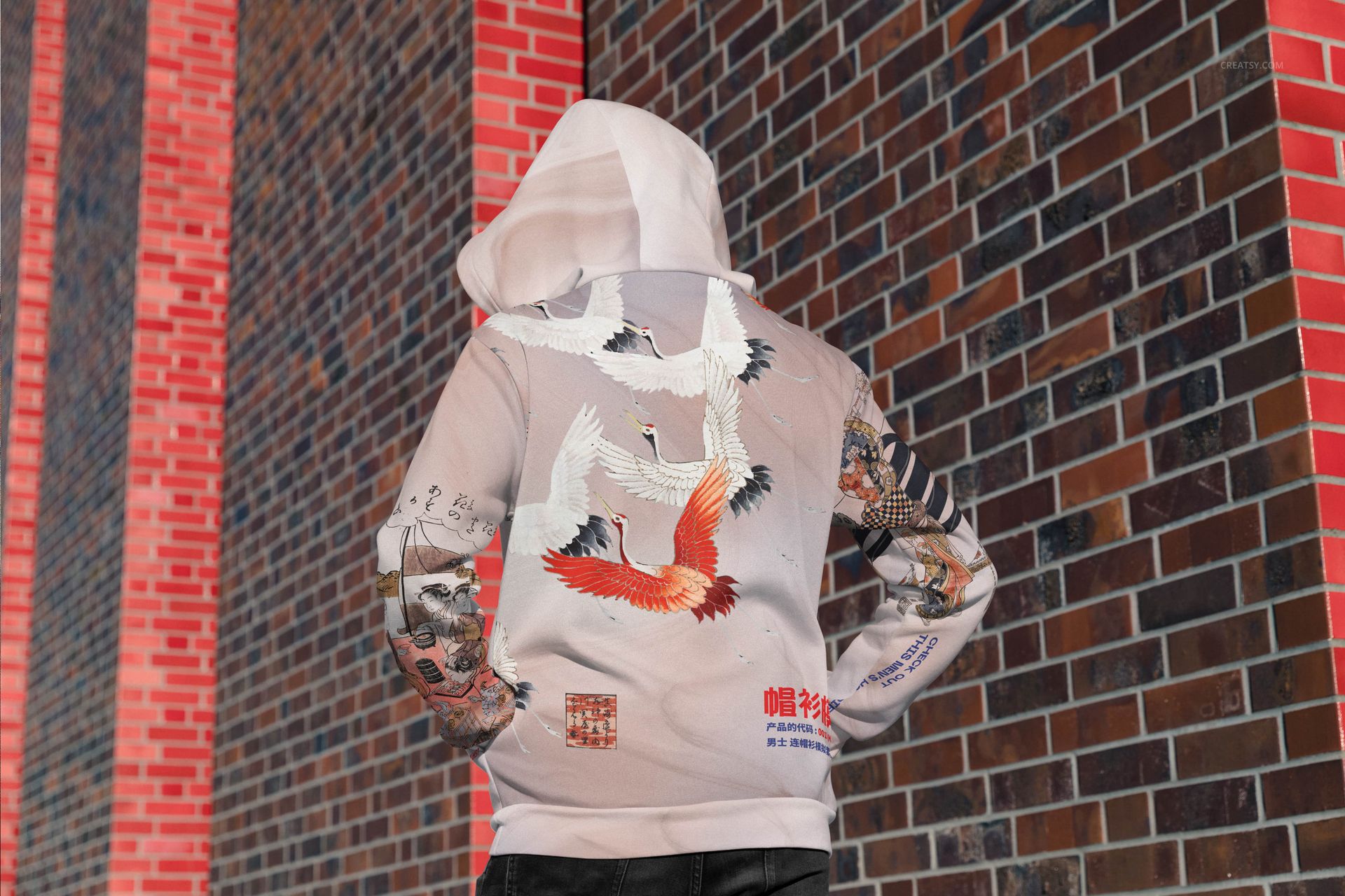 Adult-sized hoodie mockup with colorful crane artwork and tattoo-inspired designs, viewed from behind near brick walls.