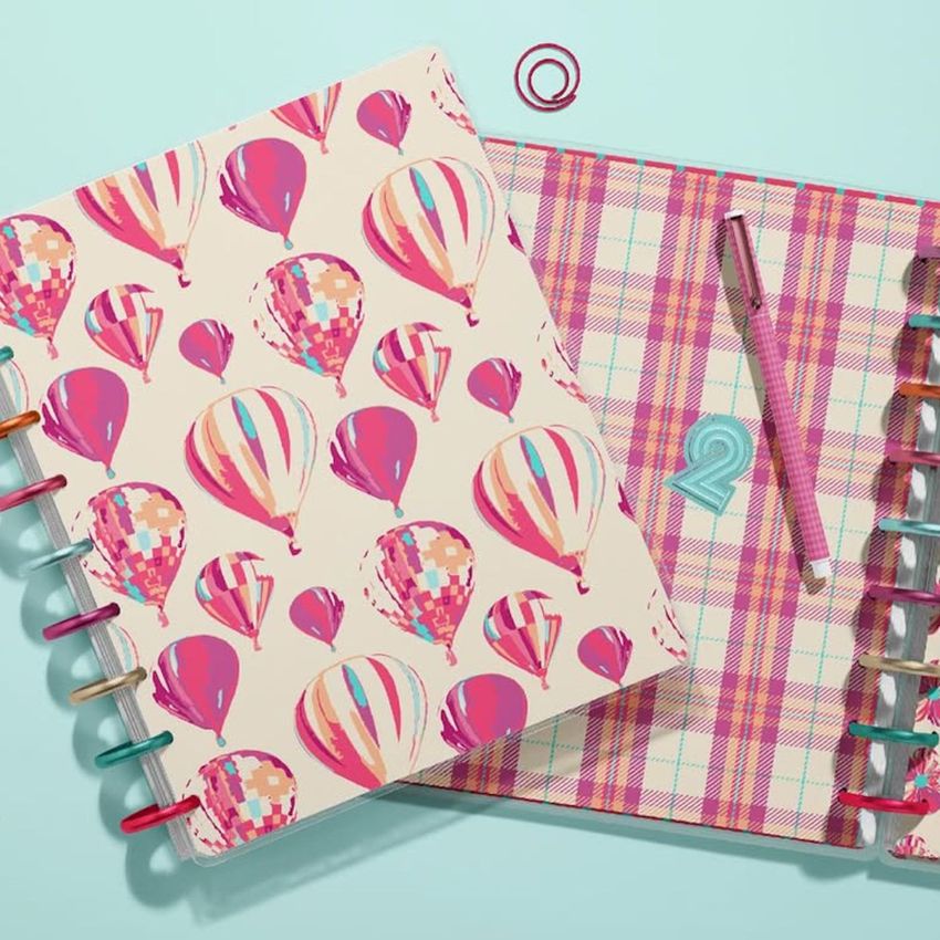 Top view of two spiral planner mockups on a light blue surface, one with colorful hot air balloon patterns and one with a pink plaid cover.