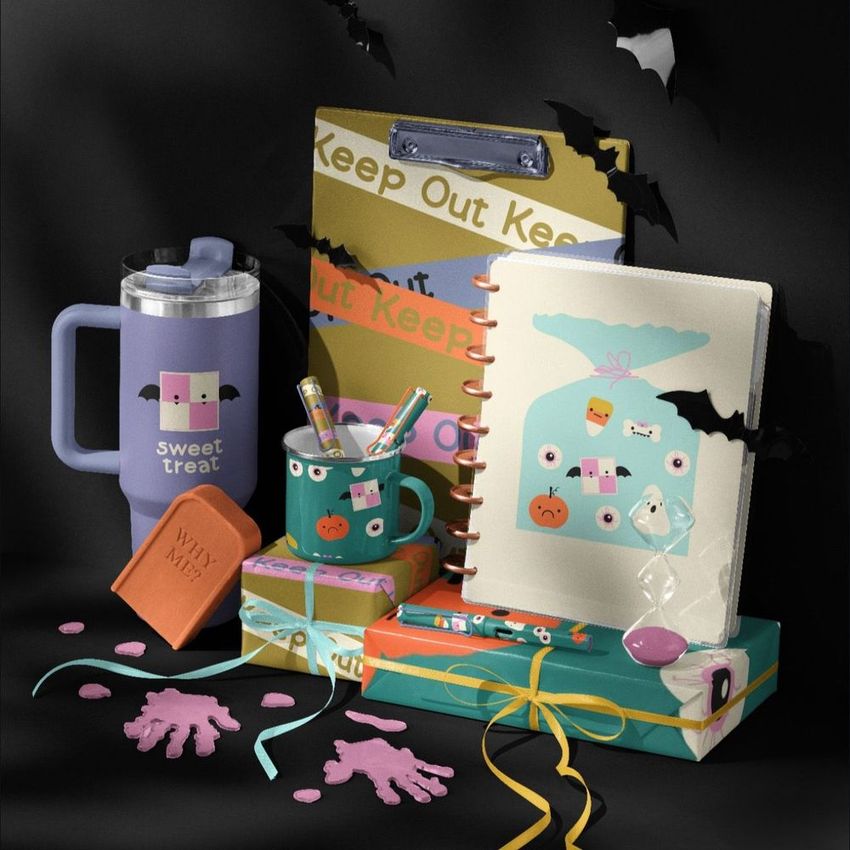 Halloween desk stationery and drinkware mockup featuring themed notebooks, mugs, and boxes with playful designs, surrounded by black paper bats on a dark background.