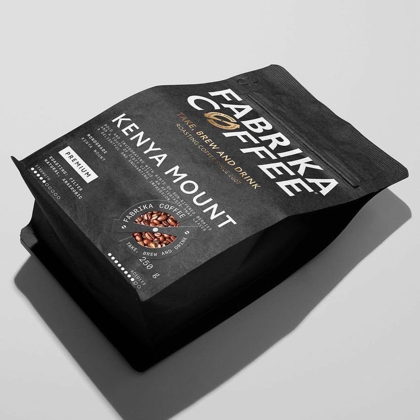 Coffee bag mockup featuring a matte black package with bold white text and a photo of coffee beans, shown on a light surface.